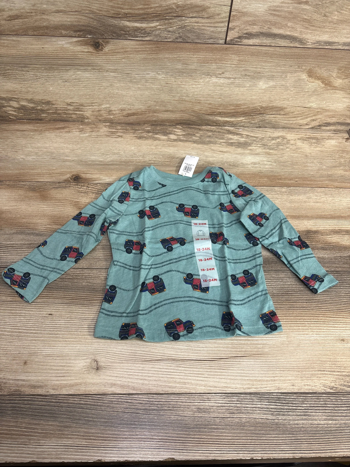Blue long sleeve toddler shirt with red truck pattern, size 18-24 months, on wood background