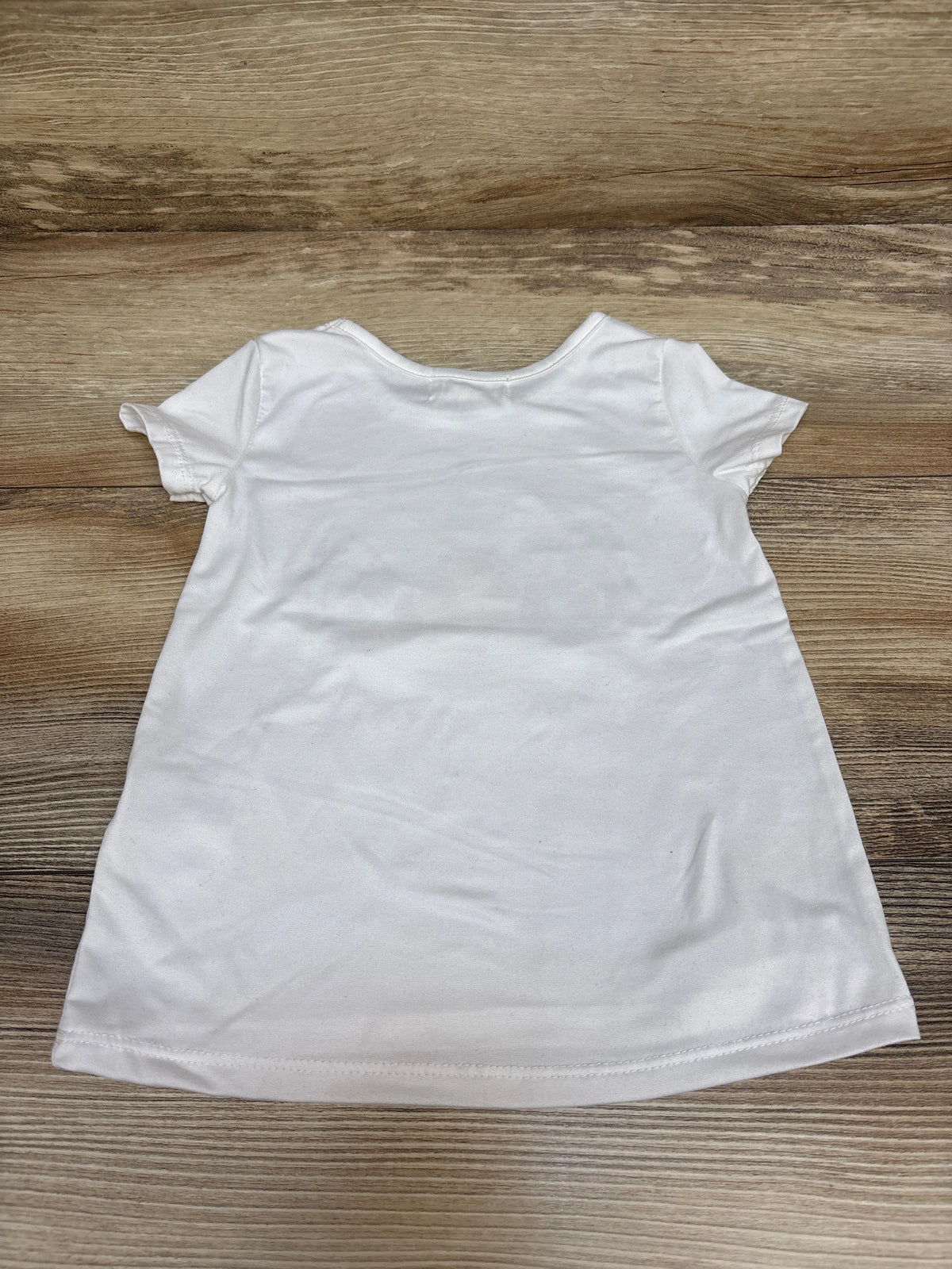 Back view of Btween unicorn shirt in white, size 2T, showcasing its short sleeves and plain back on a wood surface