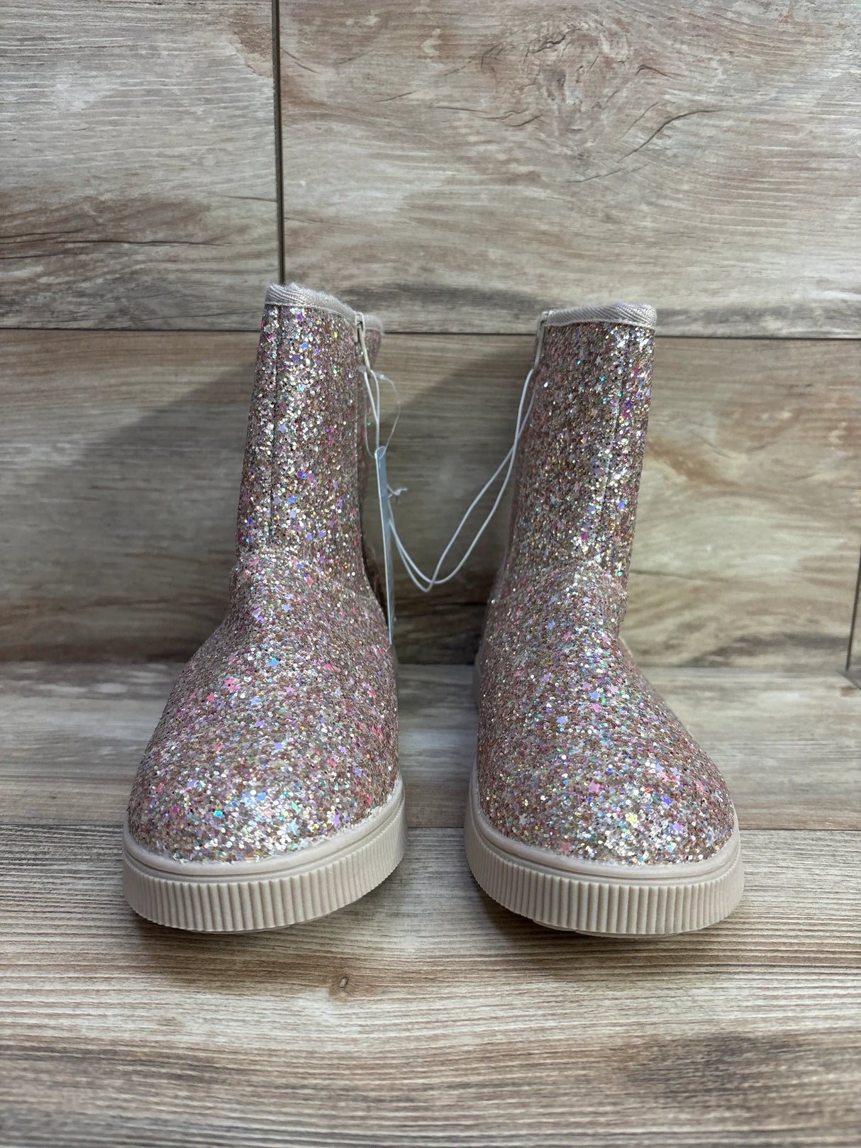 Pair of pink glittery kids ankle boots with rubber soles on wood background
