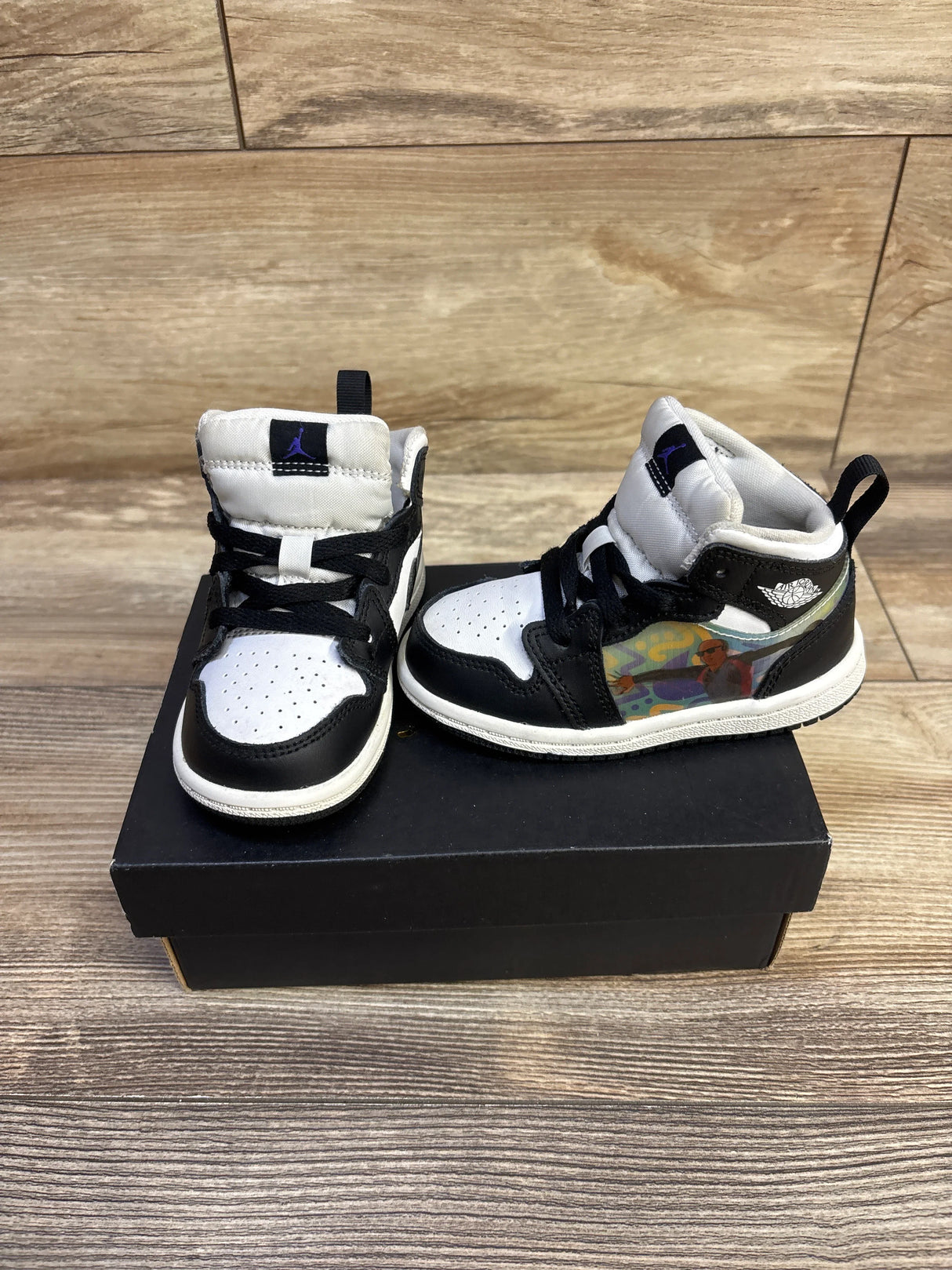 Three-quarter view of Jordan 1 Mid Hologram sneakers with black-and-white leather and holographic side panel on a black box