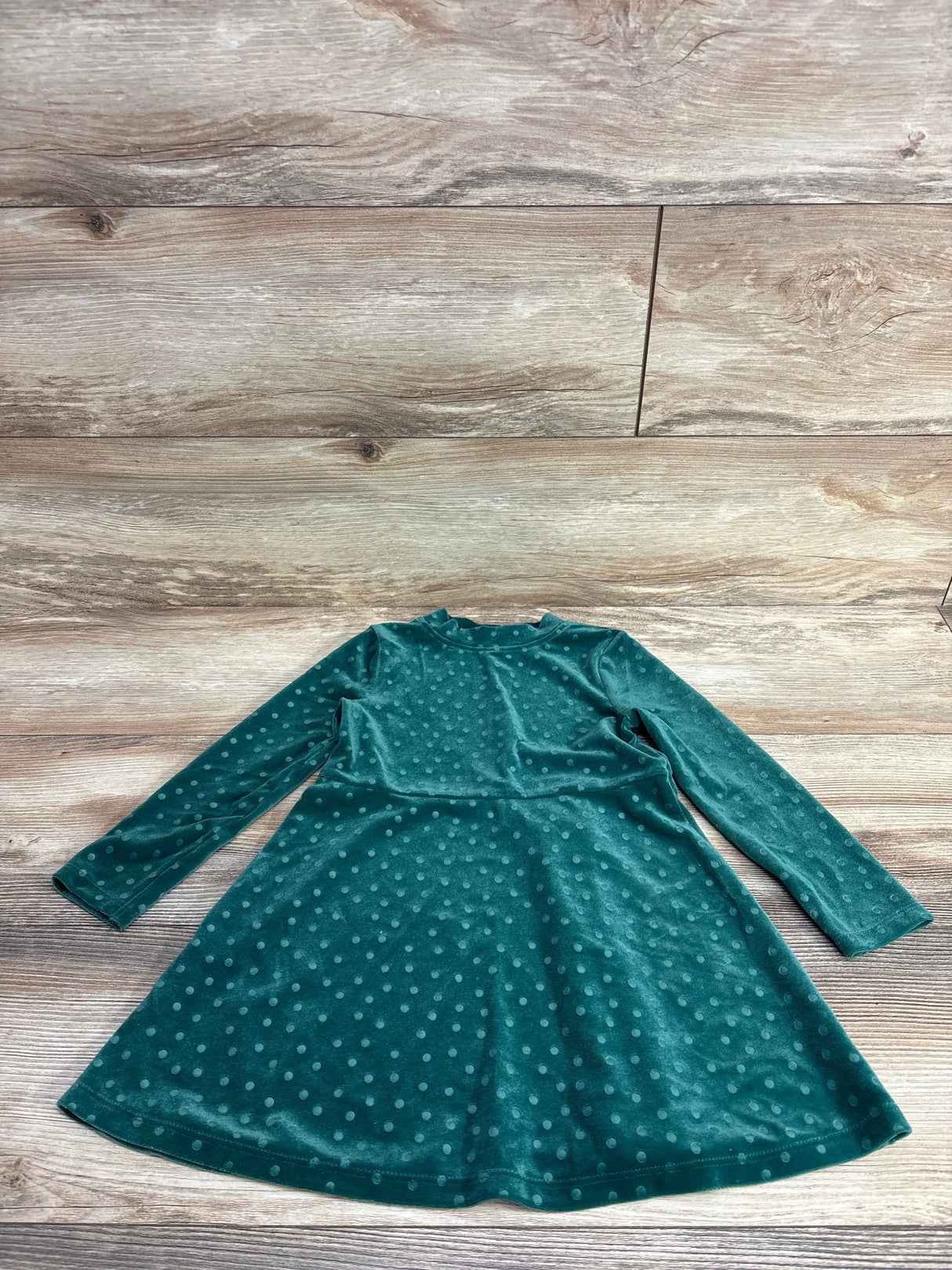 Green velvet long sleeve girls dress with polka dot pattern on wooden background
