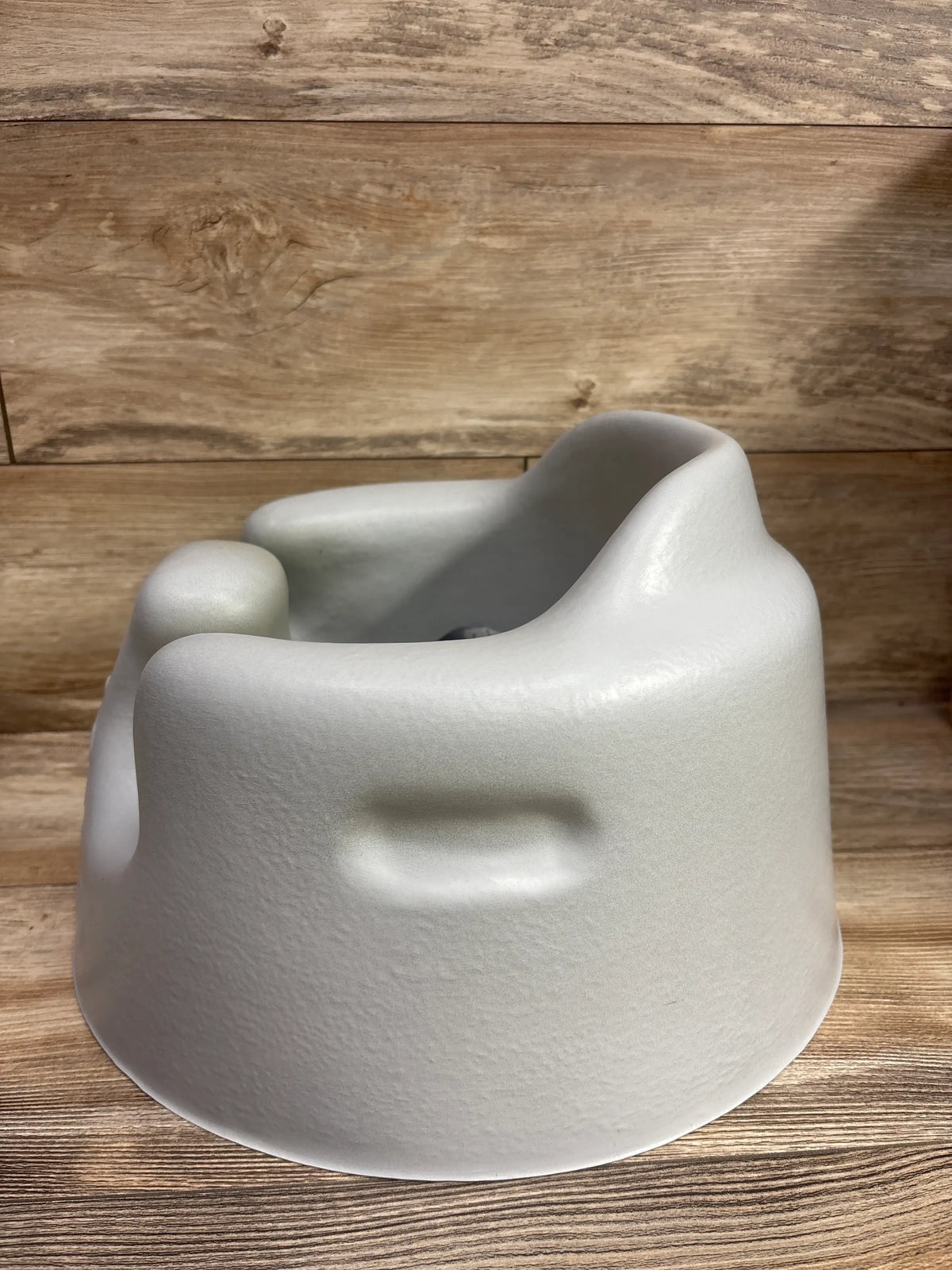 Rear three-quarter view of Bumbo Floor Seat in grey showcasing its molded seat and side handle on a wood surface