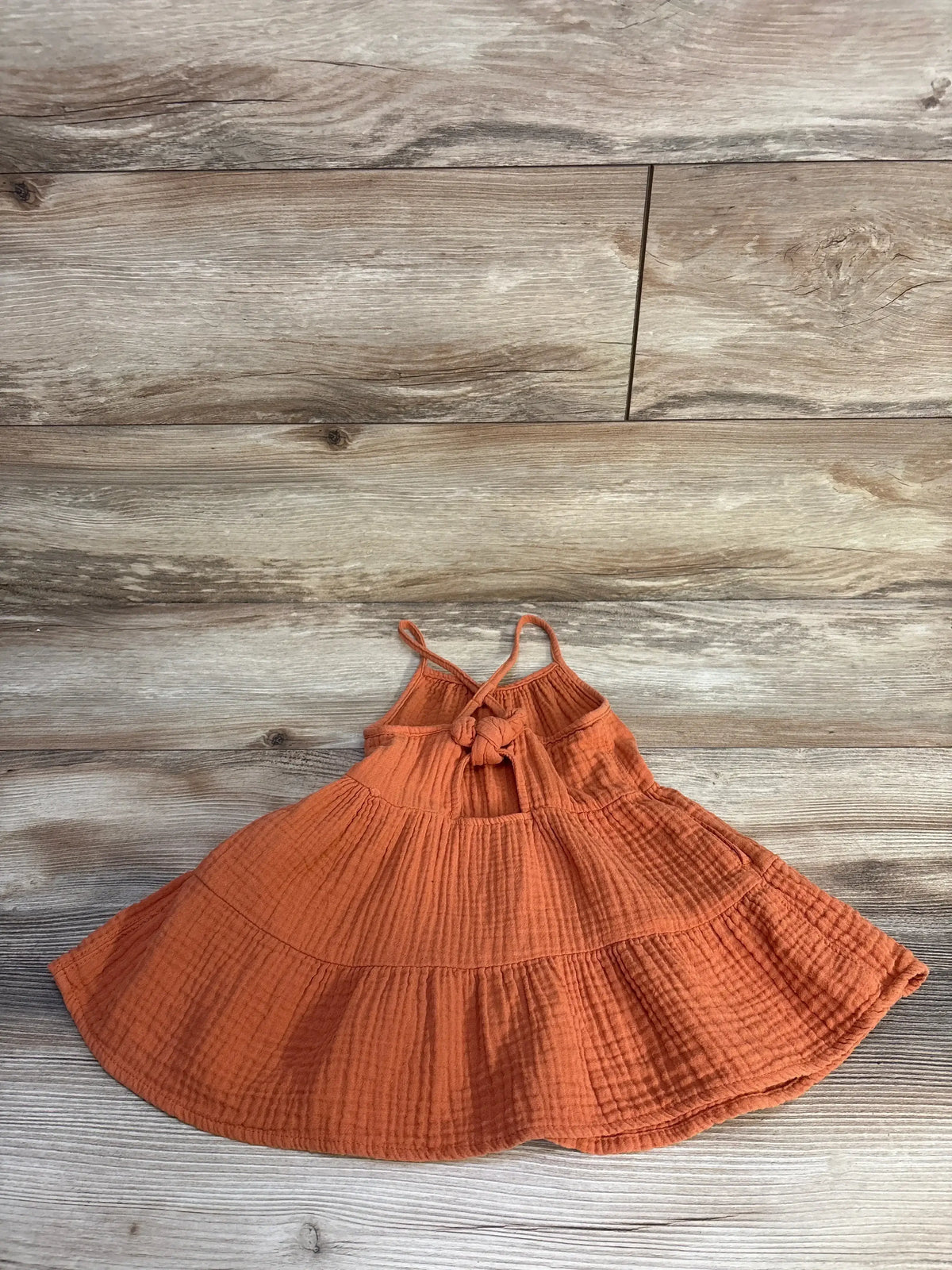 Flat lay of orange Cat & Jack gauze tiered toddler dress showing knotted back straps and three-tier ruffle on wood floor