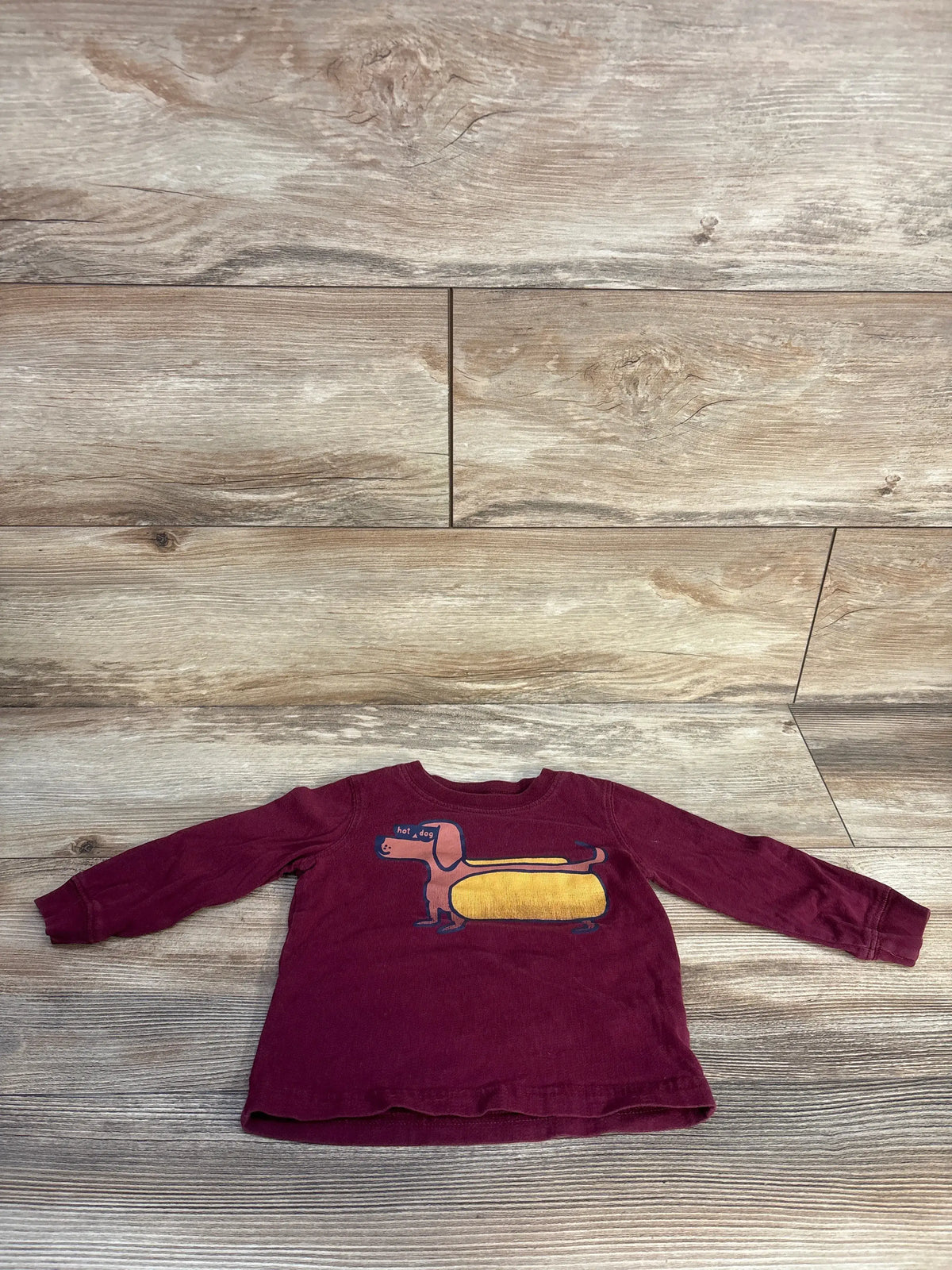 Front view of Carter’s maroon hot dog graphic shirt in size 18 months with long sleeves on a wood plank background
