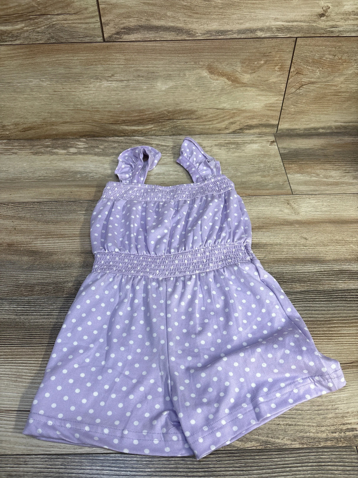 Flat-lay of purple Picapino polka-dot romper showing ruffled straps and smocked waist on wood floor