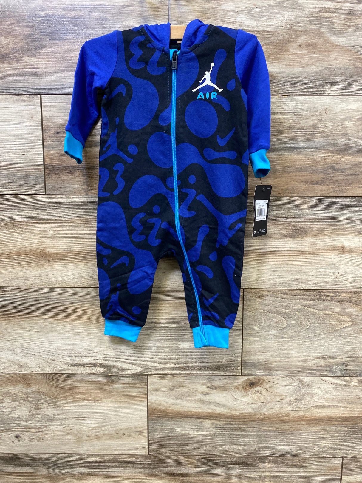 Blue and black infant jumpsuit with abstract patterns and Air Jordan logo hanging on wooden wall