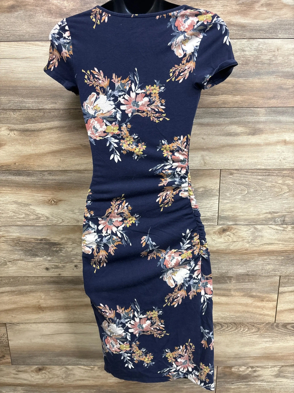 Front view of Isabel maternity floral bodycon dress in navy showing side ruching and pink-white floral print on wood-plank background