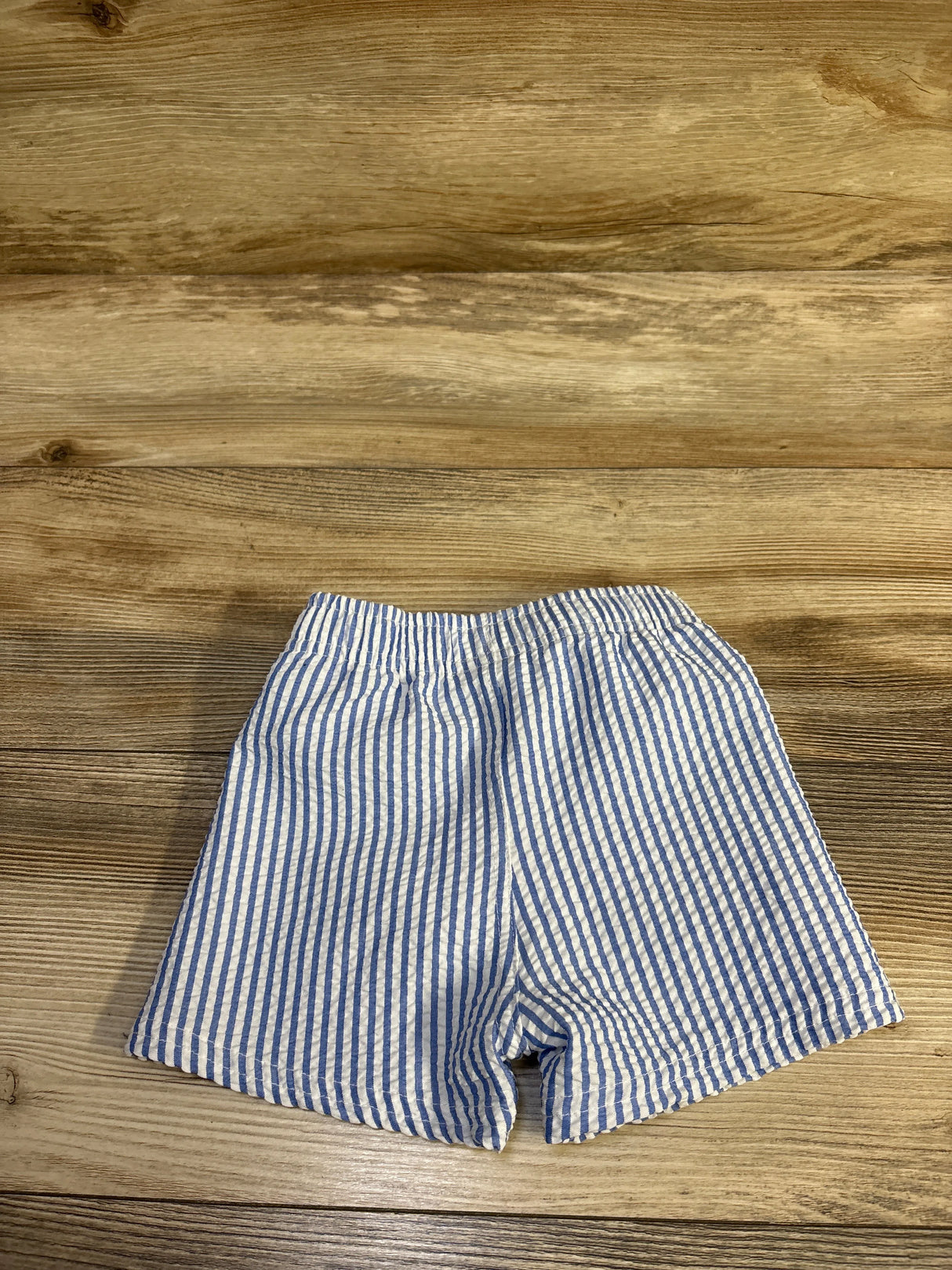 Flat lay of blue and white seersucker toddler swim shorts showing elastic waistband on wood background