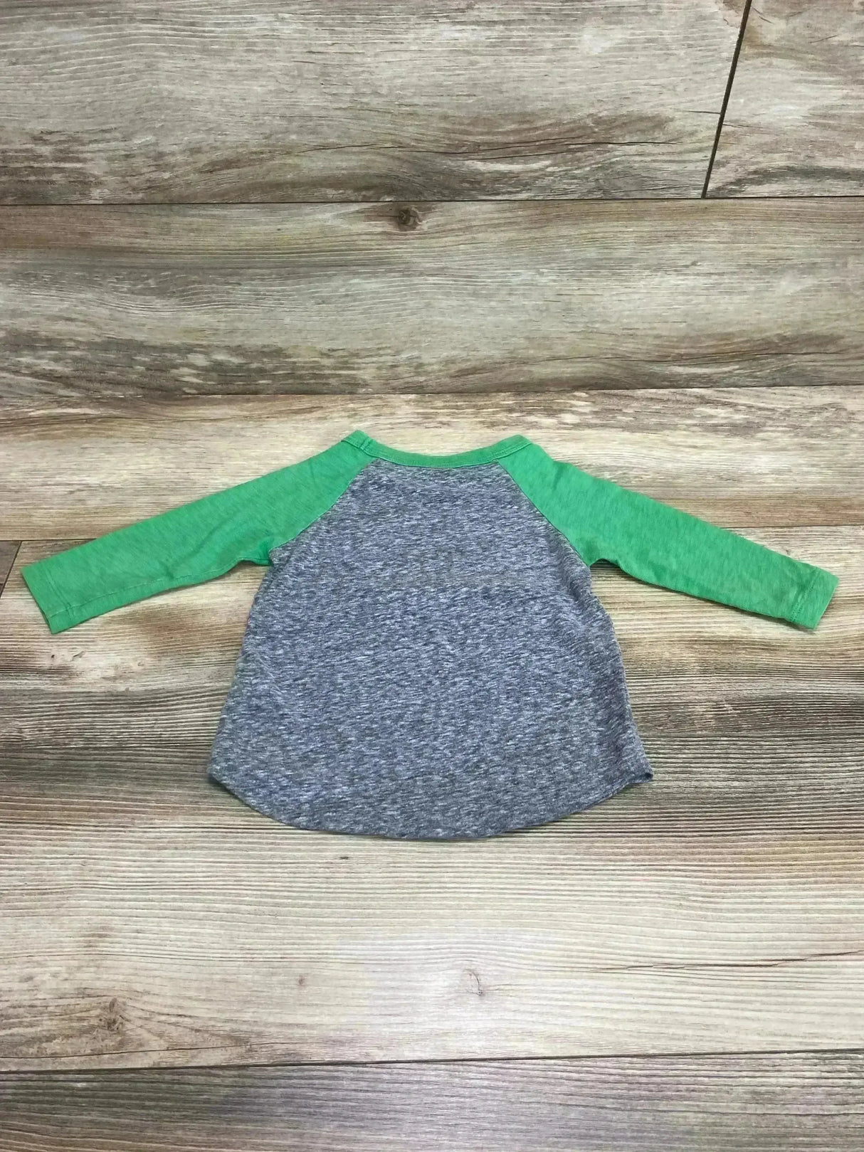 Back view of toddler raglan shirt showcasing green raglan sleeves and heather gray body, size 2T, laid flat on wood background
