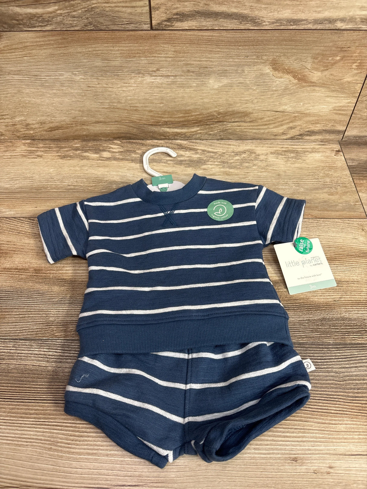 Front view of Little Planet organic navy striped shirt and matching shorts showing ribbed hem and hangtag on wood background