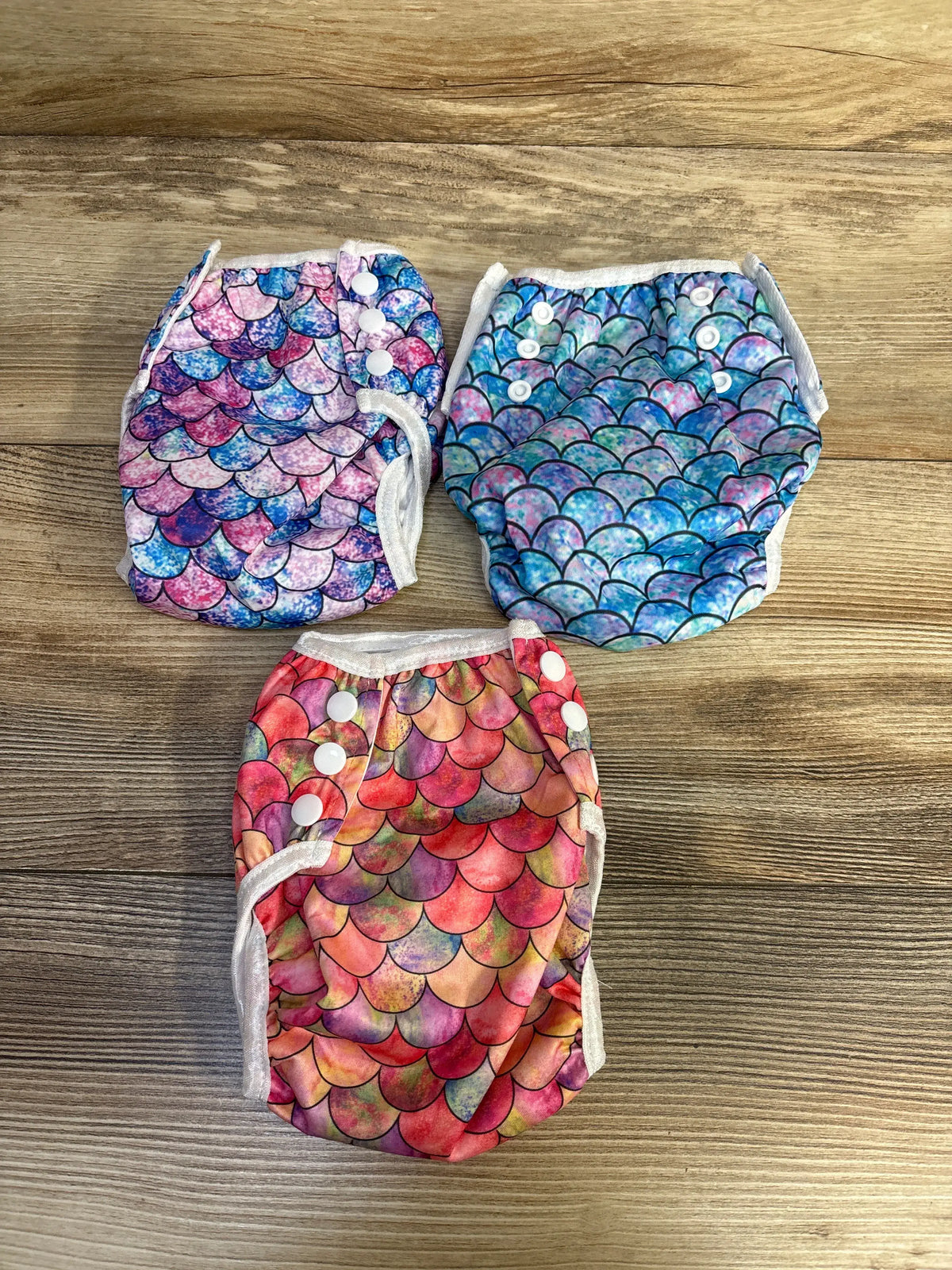 Overhead view of three Wegreeco reusable swim diapers showcasing colorful printed outer layers and adjustable snap closures on a wooden surface