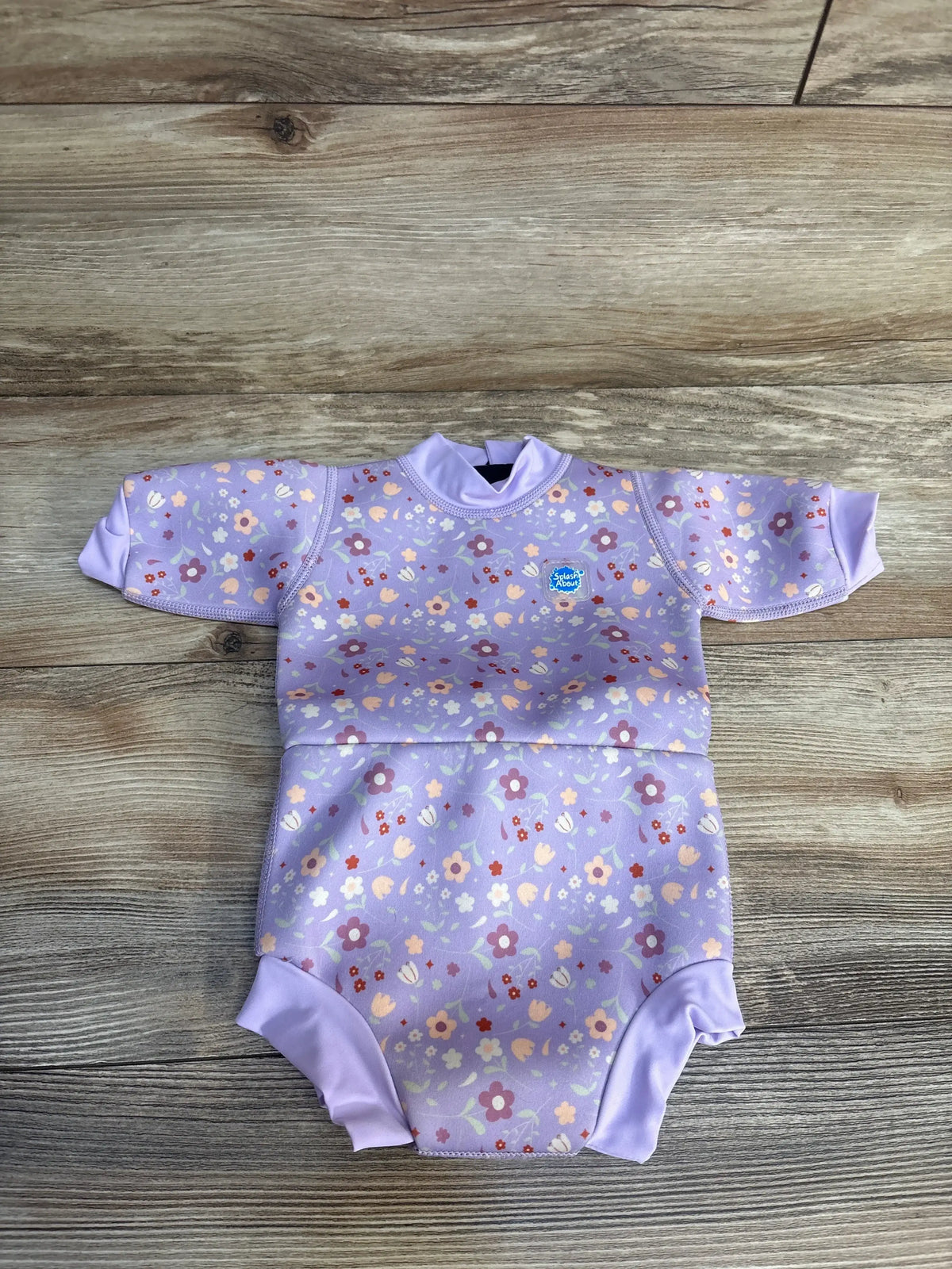 Front view of Splash About Happy Nappy Wetsuit in Lilac Spring showcasing floral print and swim diaper on wood background
