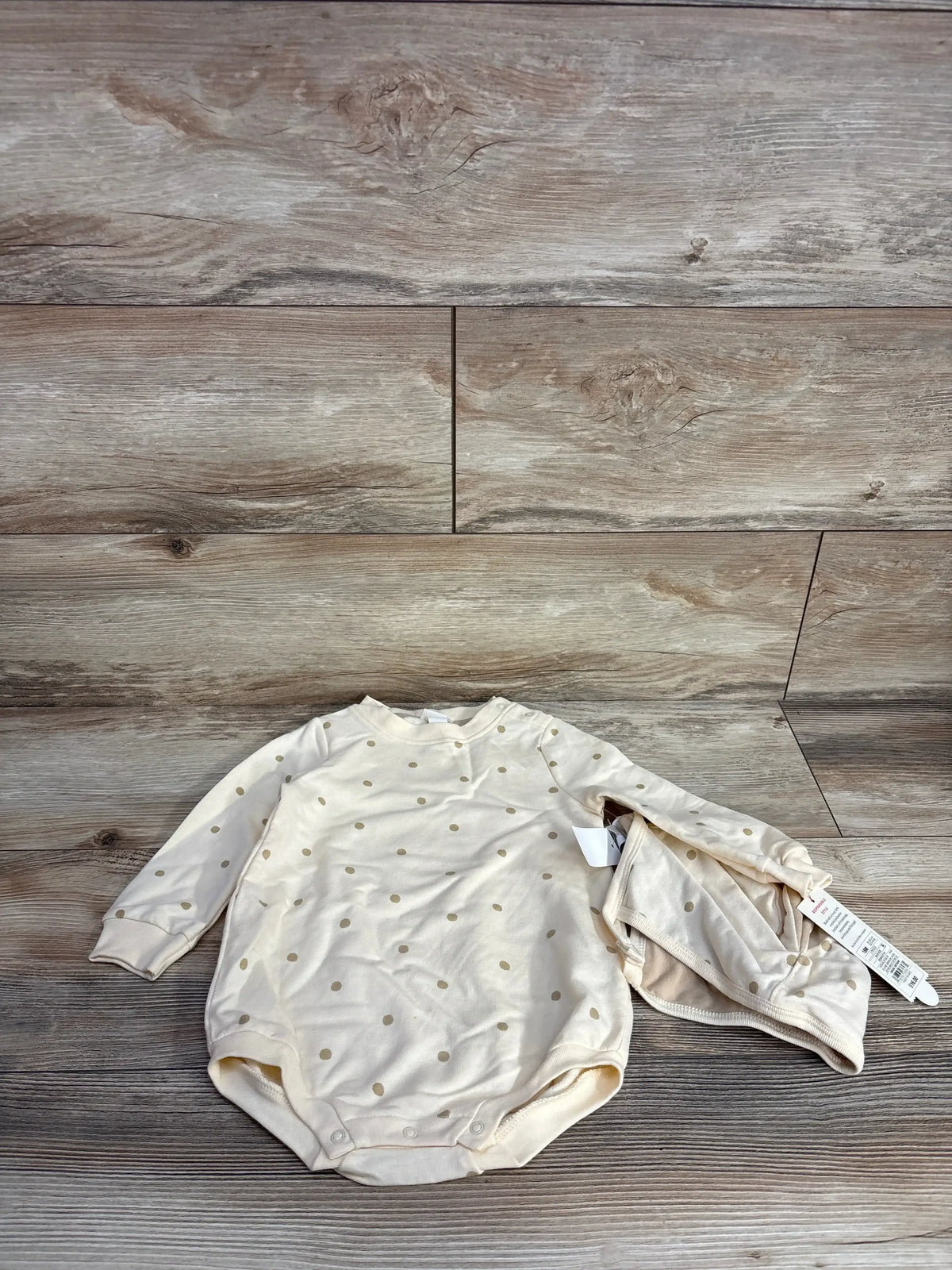 Cream-colored baby bodysuit and matching hat with gold polka dots on wood floor