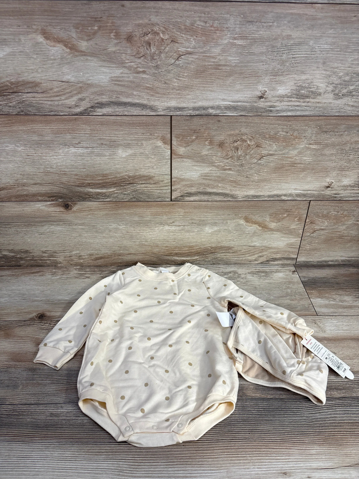 Cream-colored baby bodysuit and matching hat with gold polka dots on wood floor