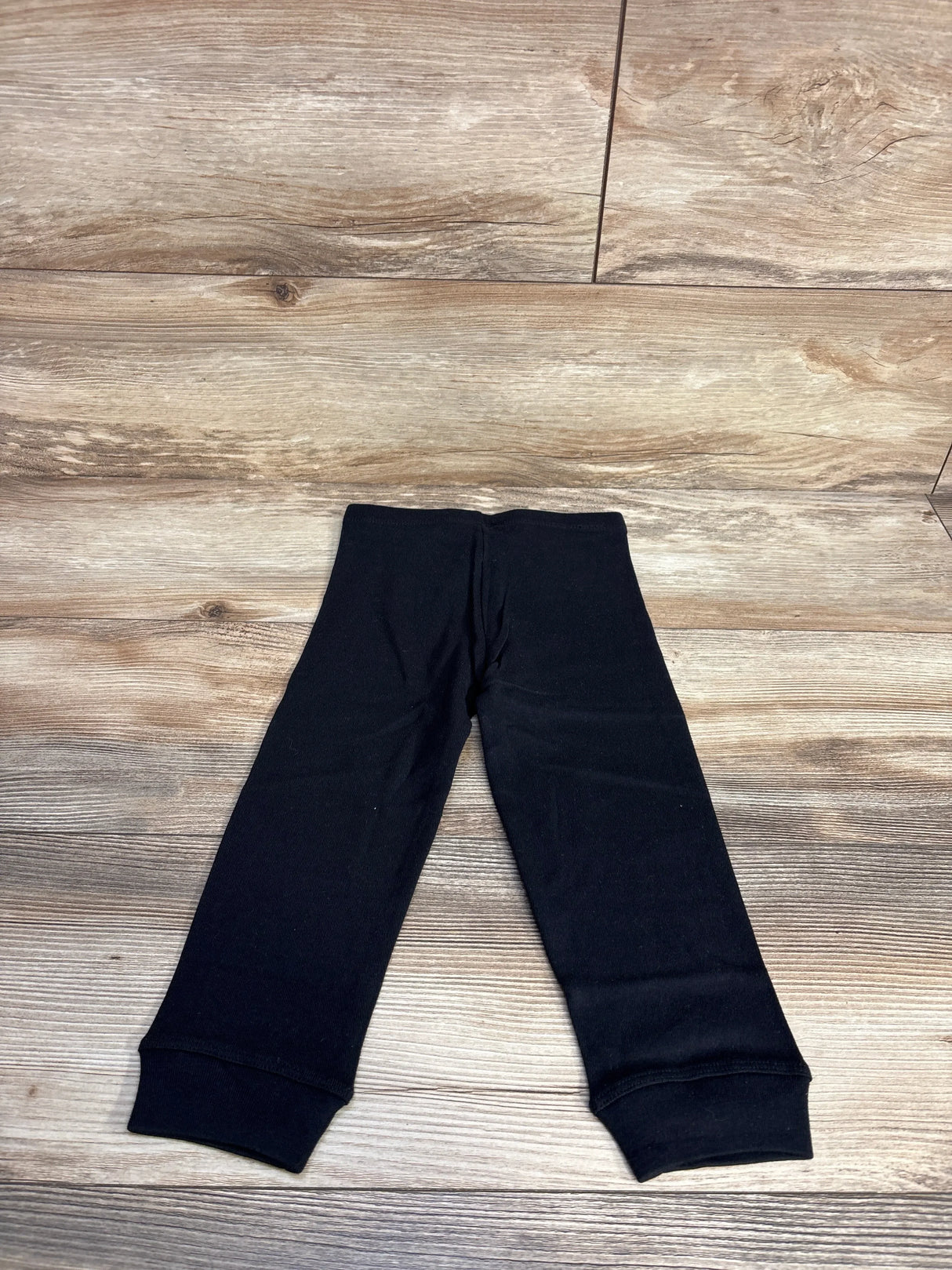 Black baby leggings with cuffed ankles laid flat on wooden floor