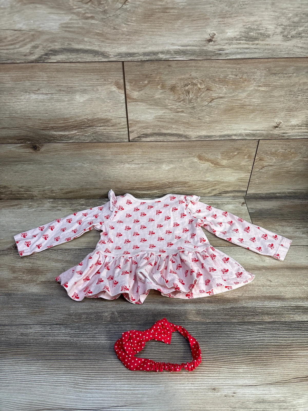 Front view of pink Minnie Mouse peplum top and matching headband showcasing long sleeves and wood-grain floor background