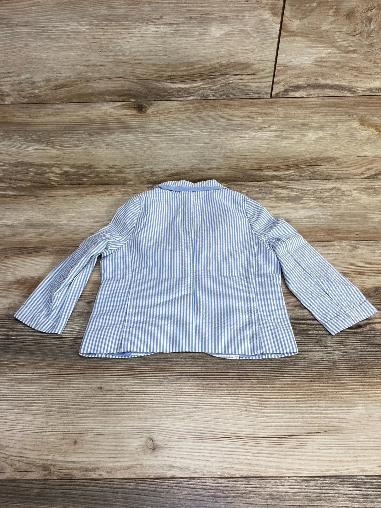 Back view of Petite Bateau toddler blazer showcasing blue and white vertical stripes and long sleeves on wood plank floor background