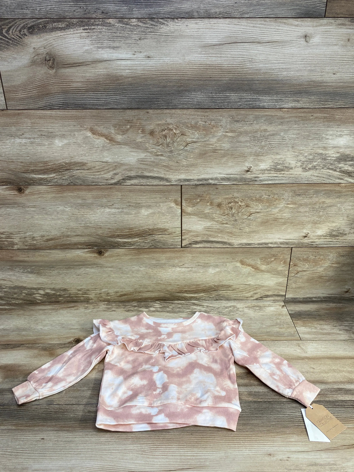 Pink and white tie-dye toddler sweater with ruffle detail on wooden background