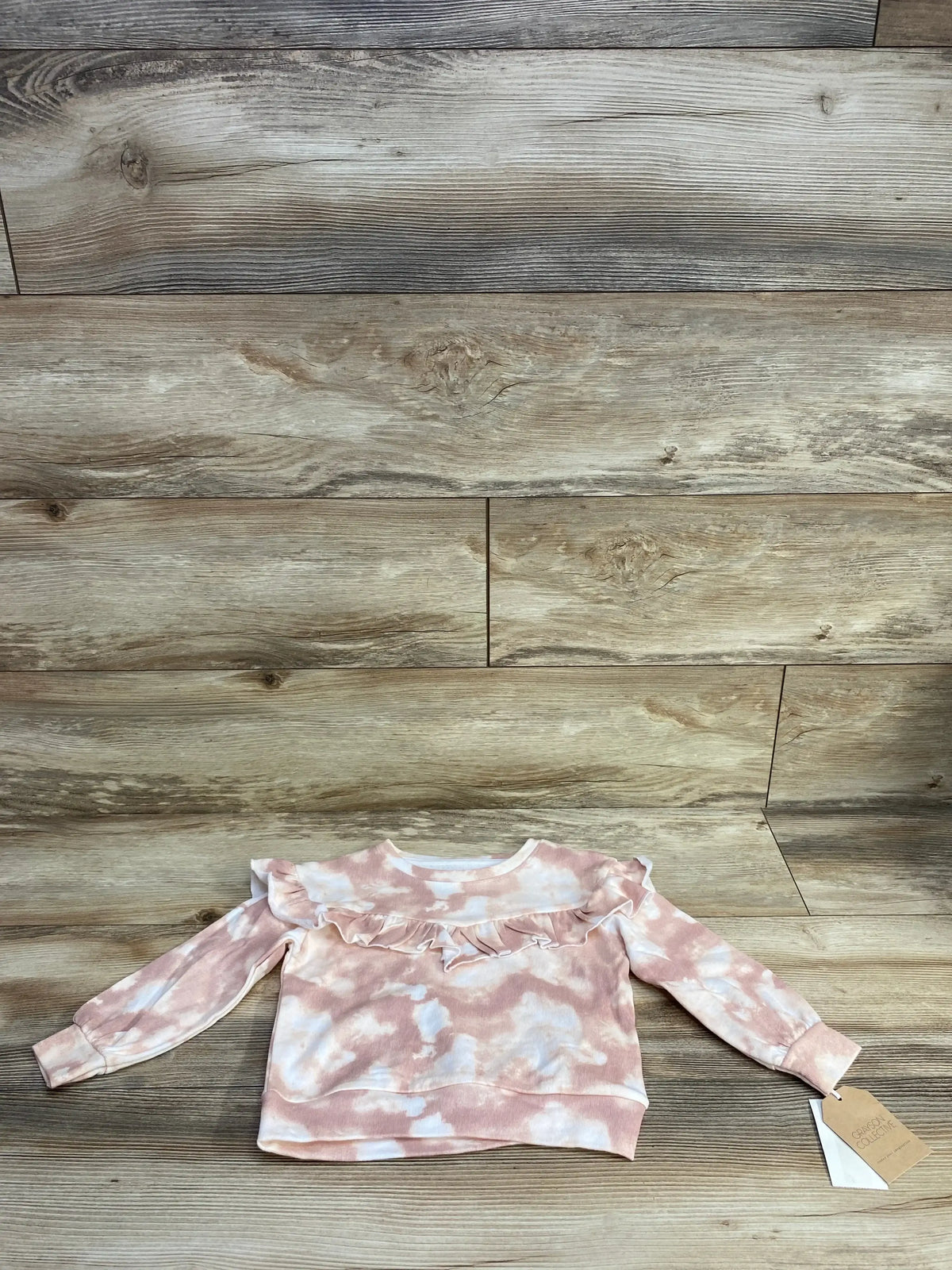Pink and white tie-dye toddler sweater with ruffle detail on wooden background