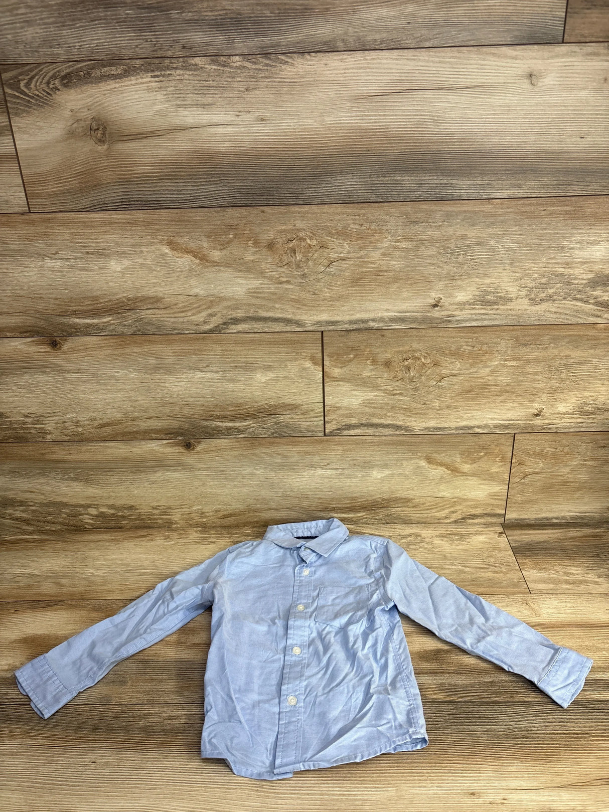 Light blue long sleeve kids button-up shirt on wooden floor, gently used children's clothing