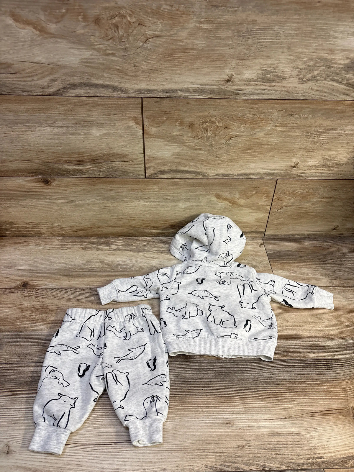 Top-down view of Carter’s 2-piece grey zip-up jacket and pants set with animal print, hood, and ribbed cuffs on wood