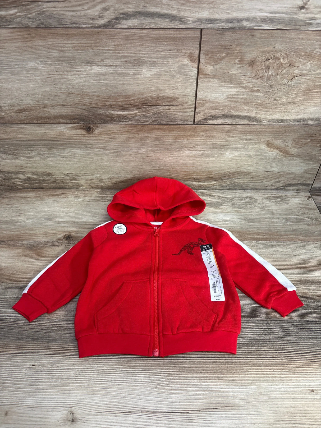 Red toddler zip-up hoodie with dinosaur graphic, white sleeve stripes, and tags displayed