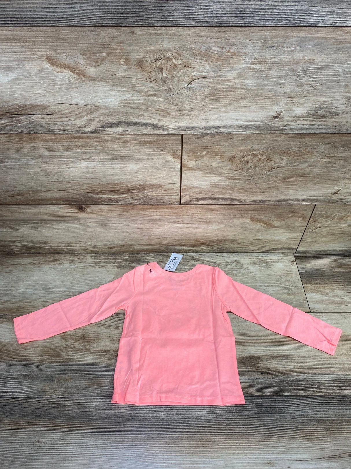 Light pink long-sleeve toddler shirt laid flat on rustic wooden floor background