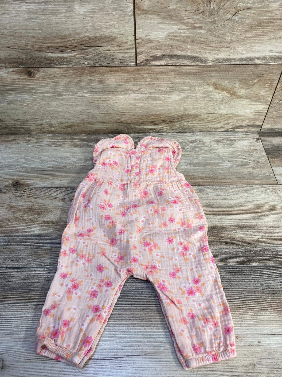 Flat lay of pink Cat and Jack gauze jumpsuit with collared top, ruffle straps, floral print and elasticized ankles on wood background