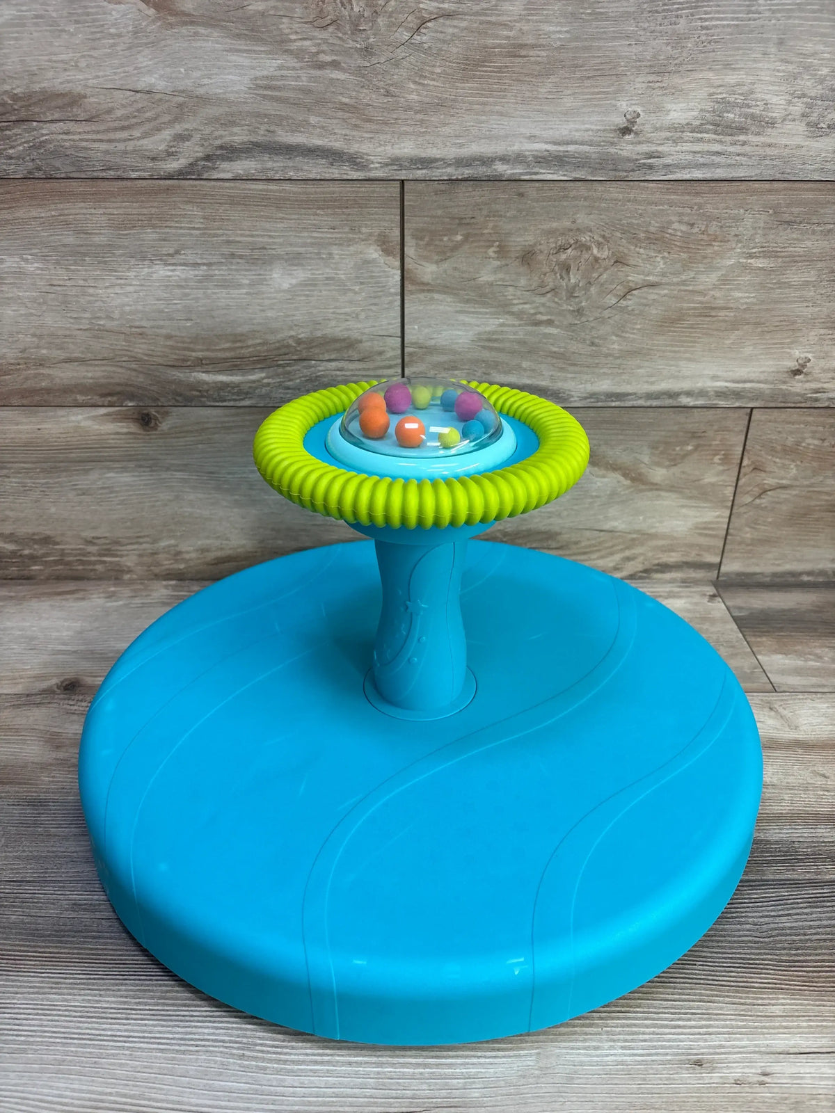 Angled top view of B Toys Twirly Time showing green spinning ring and clear dome with colorful balls on a blue base