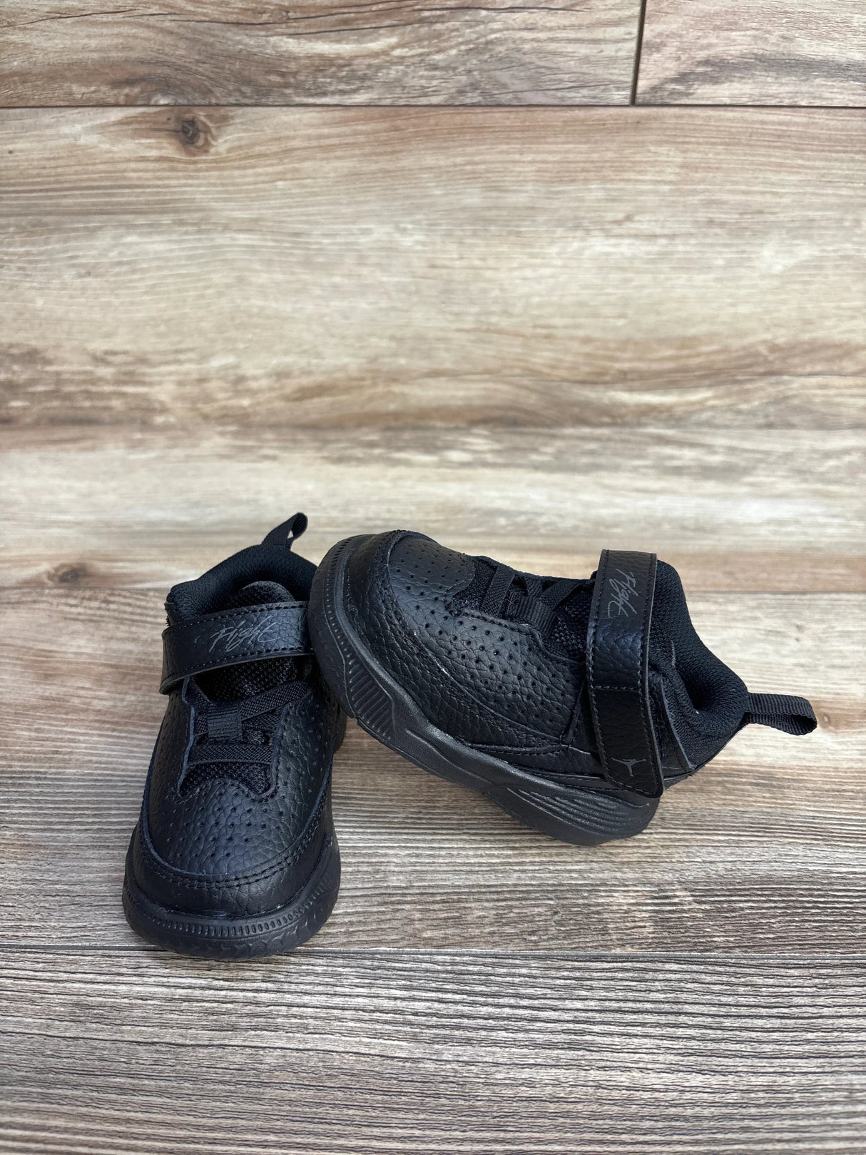 Three-quarter view of Air Jordan Max Aura 5 TD toddler sneakers, Black Anthracite, showing perforated upper and Velcro strap on wood floor
