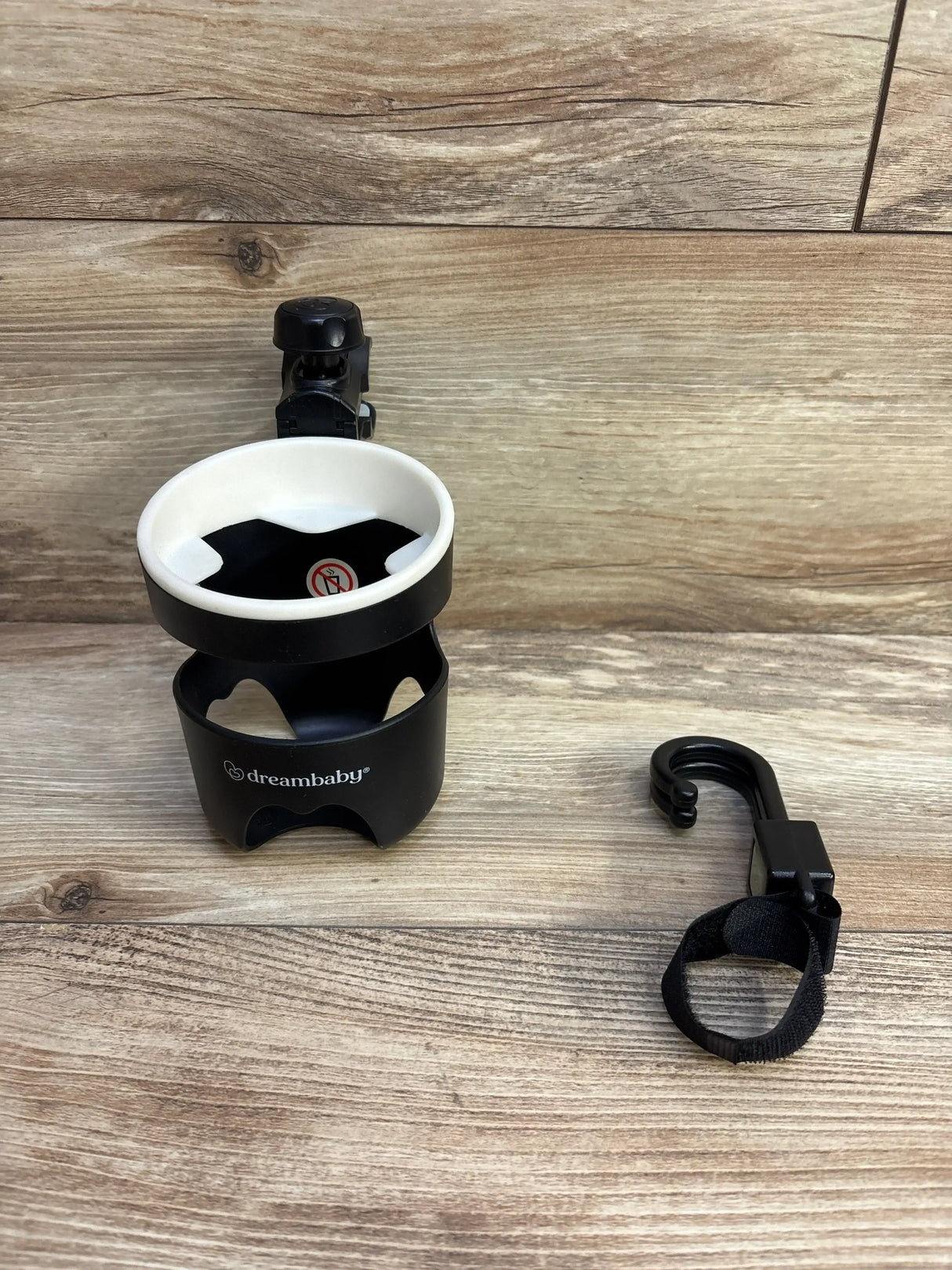 Flat lay of Dreambaby 2pc stroller hook and bottle holder showcasing black cup holder with white interior and clip hook on wood plank floor