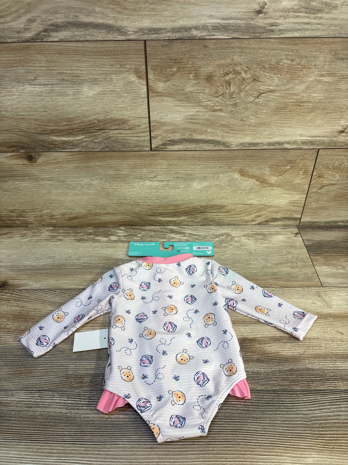 Disney Baby Winnie the Pooh long-sleeve onesie with pink trim, honey pot print, on wood floor
