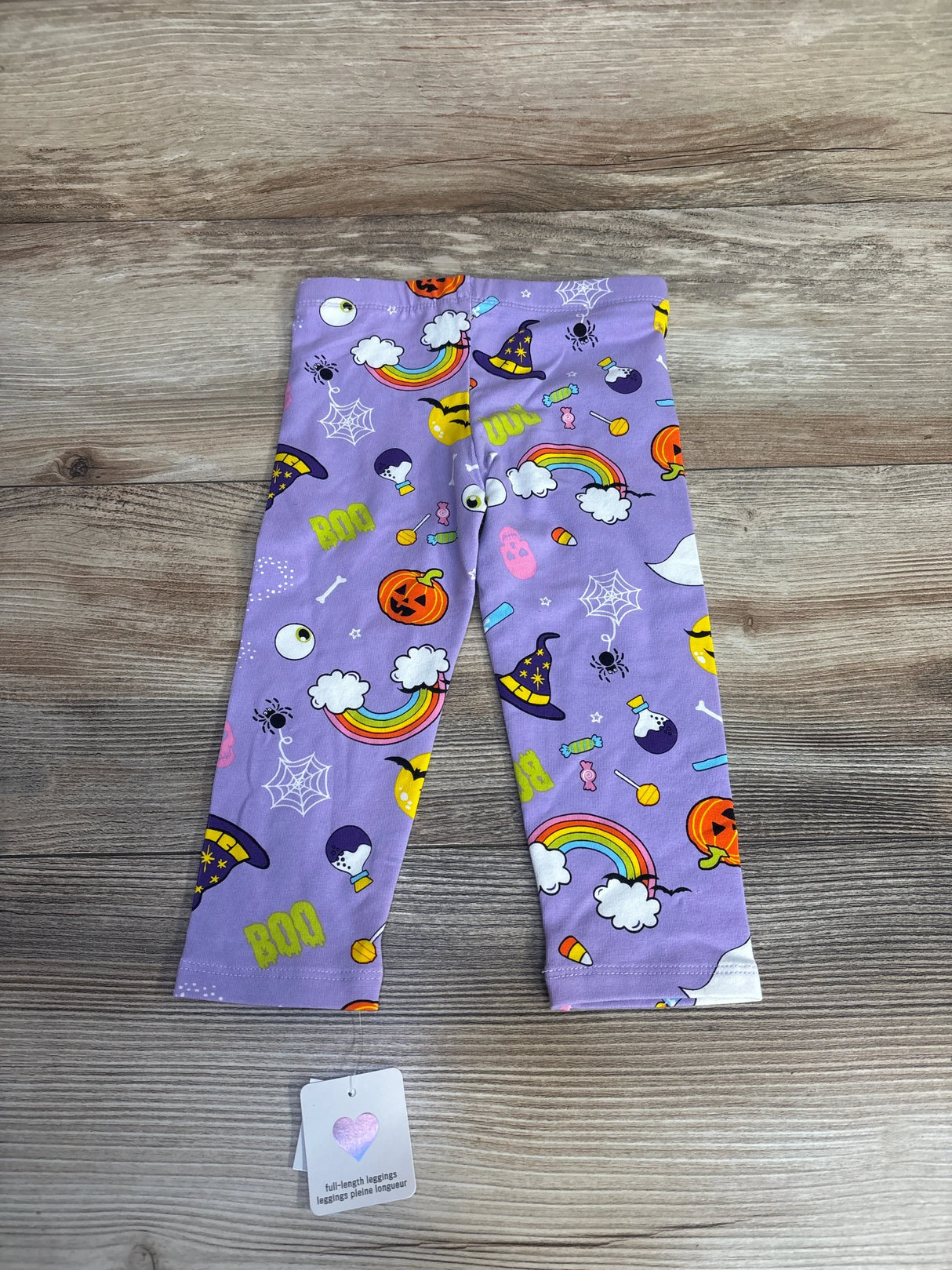 Purple Halloween leggings for kids with witch hats, pumpkins, rainbows, and BOO print on wood floor