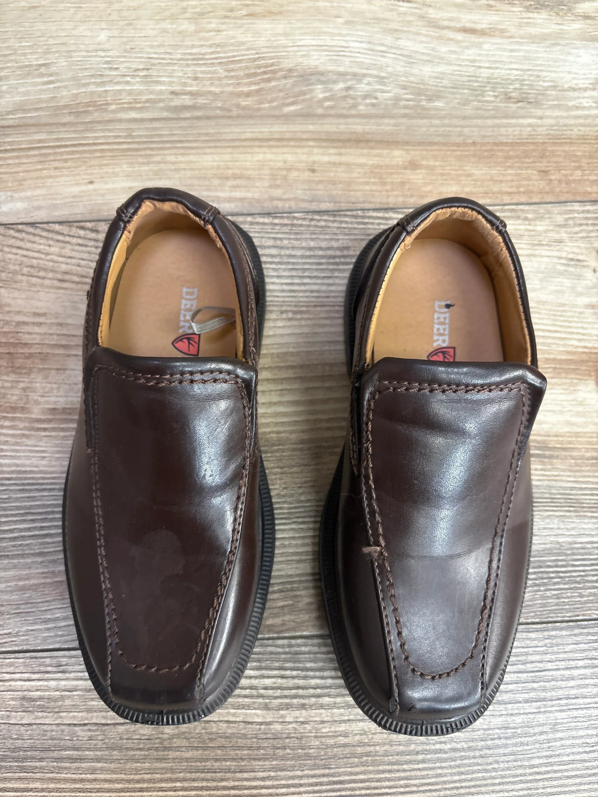 Pair of brown leather children's slip-on shoes on wooden floor, branded Deer Stags, gently used