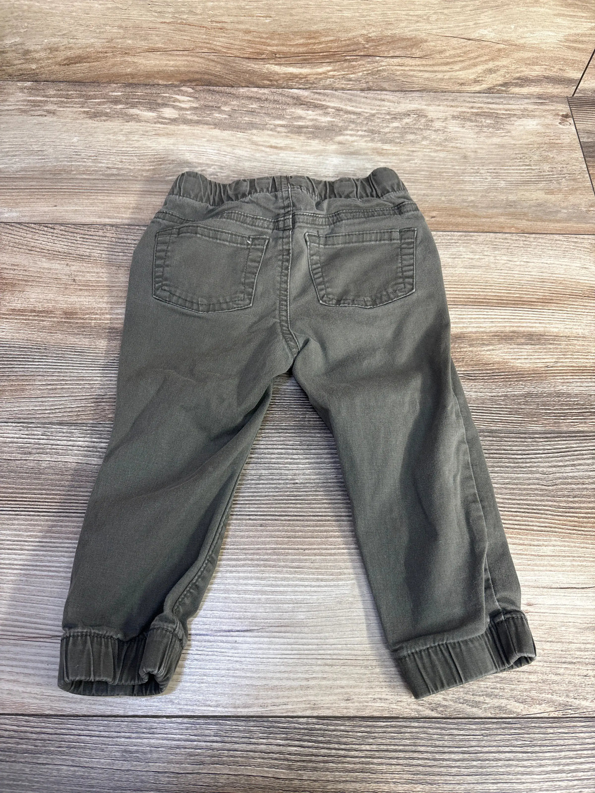 Back view of green Cat & Jack drawstring joggers showcasing back pockets and elastic cuffs on a wood-grain background