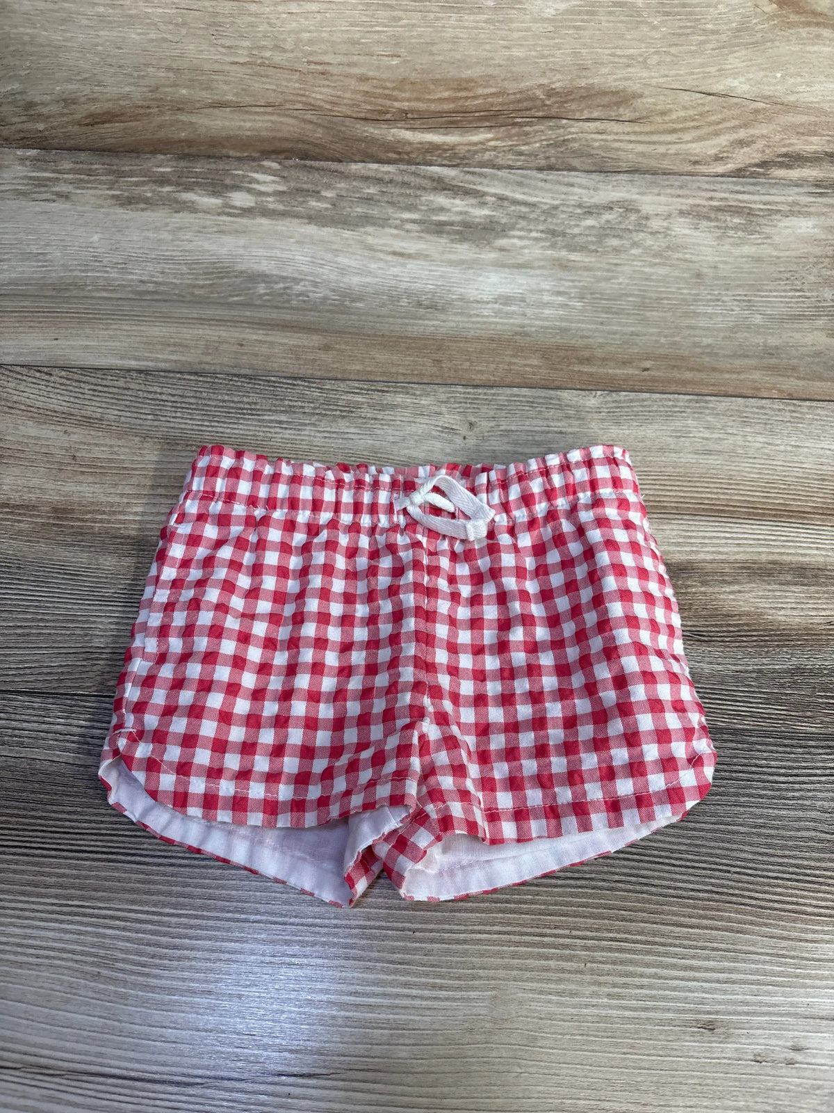 Front view of Cat & Jack red gingham shorts showcasing gathered waistband and white drawstring on a woodgrain surface
