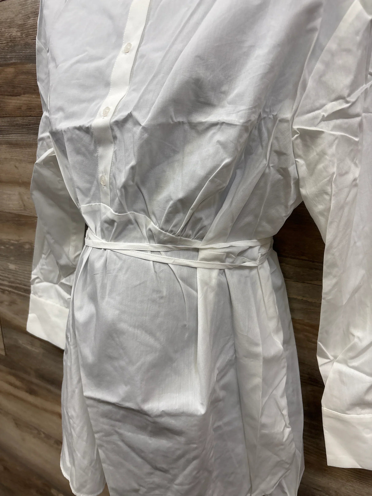 White button-down long sleeve dress with waist tie, displayed against wood background
