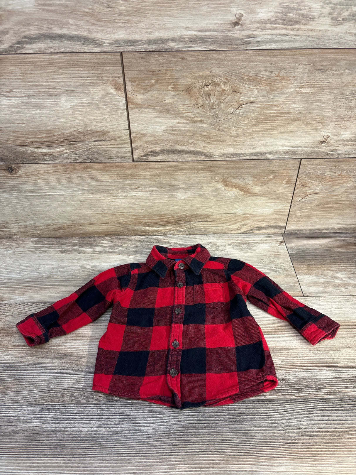 Red and black plaid baby flannel shirt with buttons on wood floor background