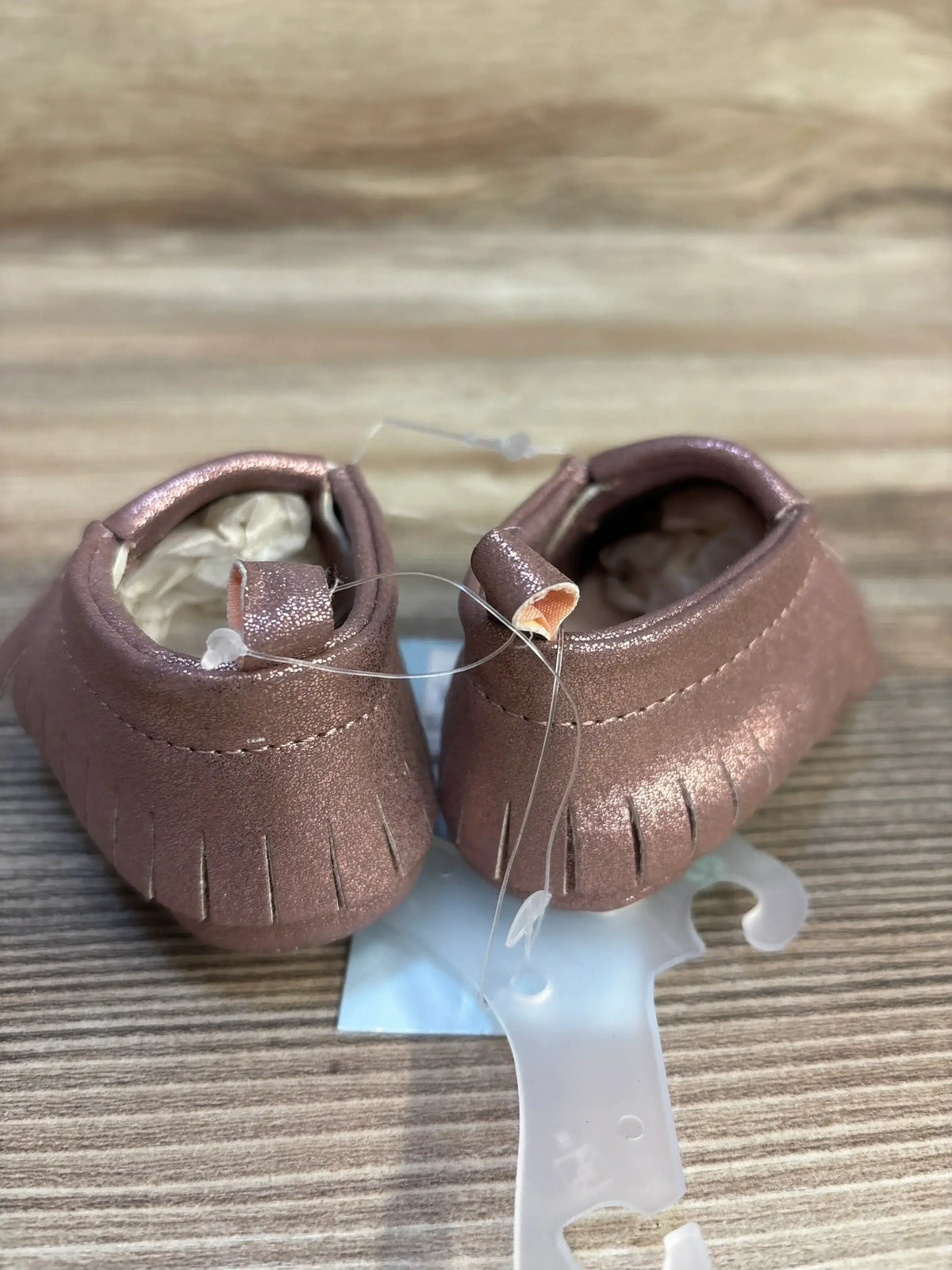 Rose gold baby moccasins with fringe detail on wood surface, kids footwear resale