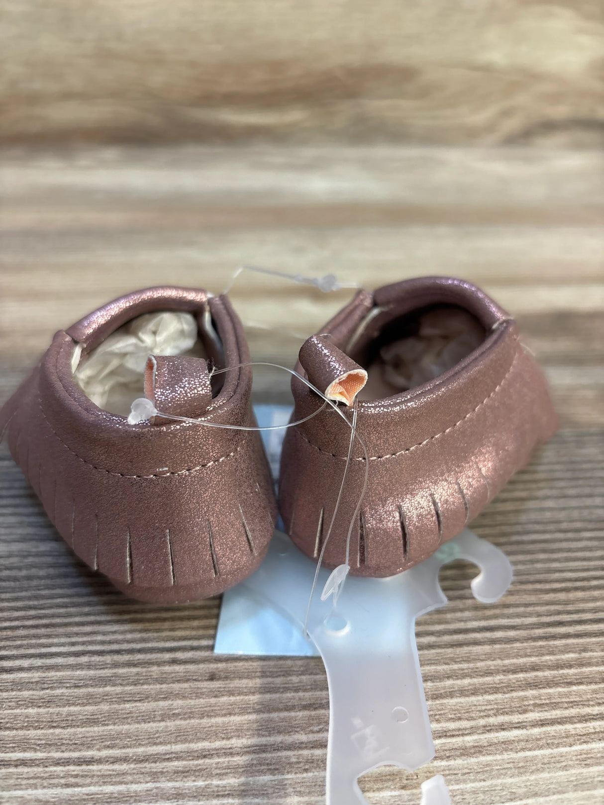 Rose gold baby moccasins with fringe detail on wood surface, kids footwear resale