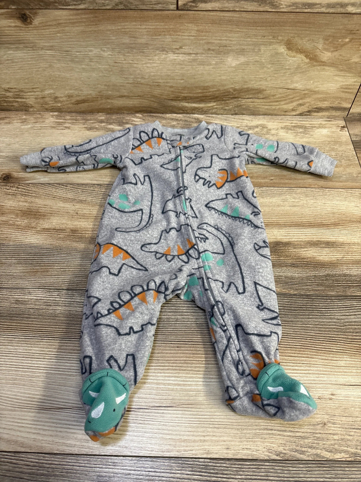 Flat-lay of grey footed blanket sleeper with dinosaur print, front zipper, and teal feet on wood