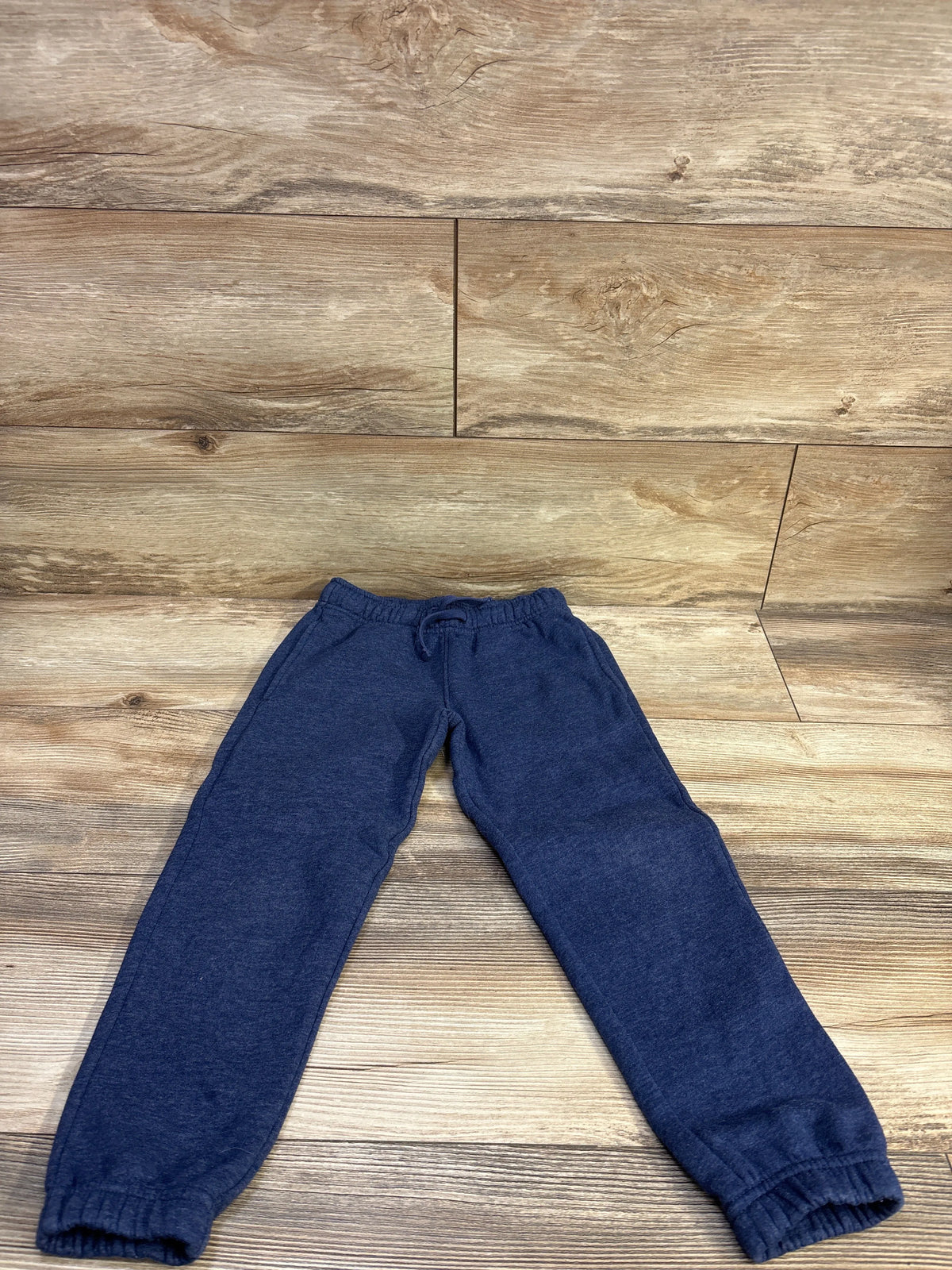 Top-down view of navy toddler drawstring joggers showing elastic waistband with drawstring and cuffed ankles on wood floor