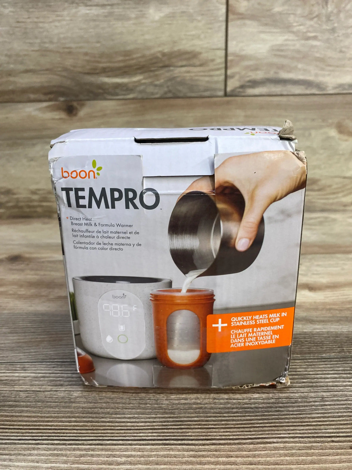 Front view of Boon Tempro breastmilk warmer box showing product image, 98.6 F digital display, and milk pouring into a stainless steel cup on a wood surface