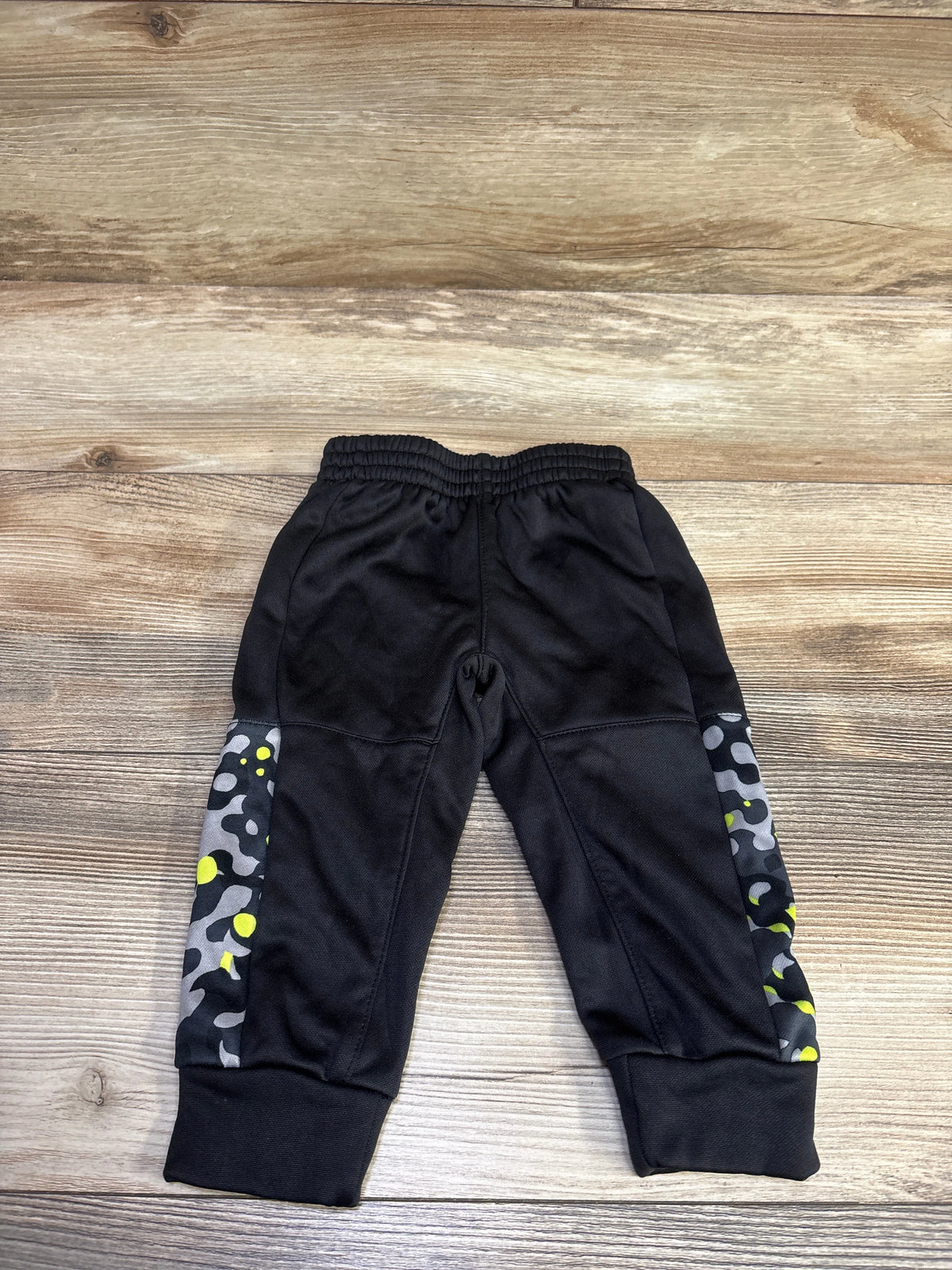Front view of Athletic Works black pull on joggers with patterned gray and neon yellow side panels and ribbed cuffs on wood