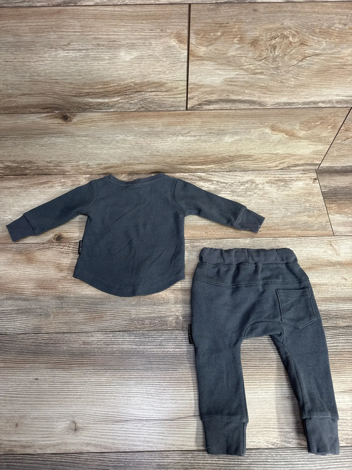 Flat lay of Little Bipsy waffle top and jogger set in shadow gray showing waffle texture and back pocket on wooden floor