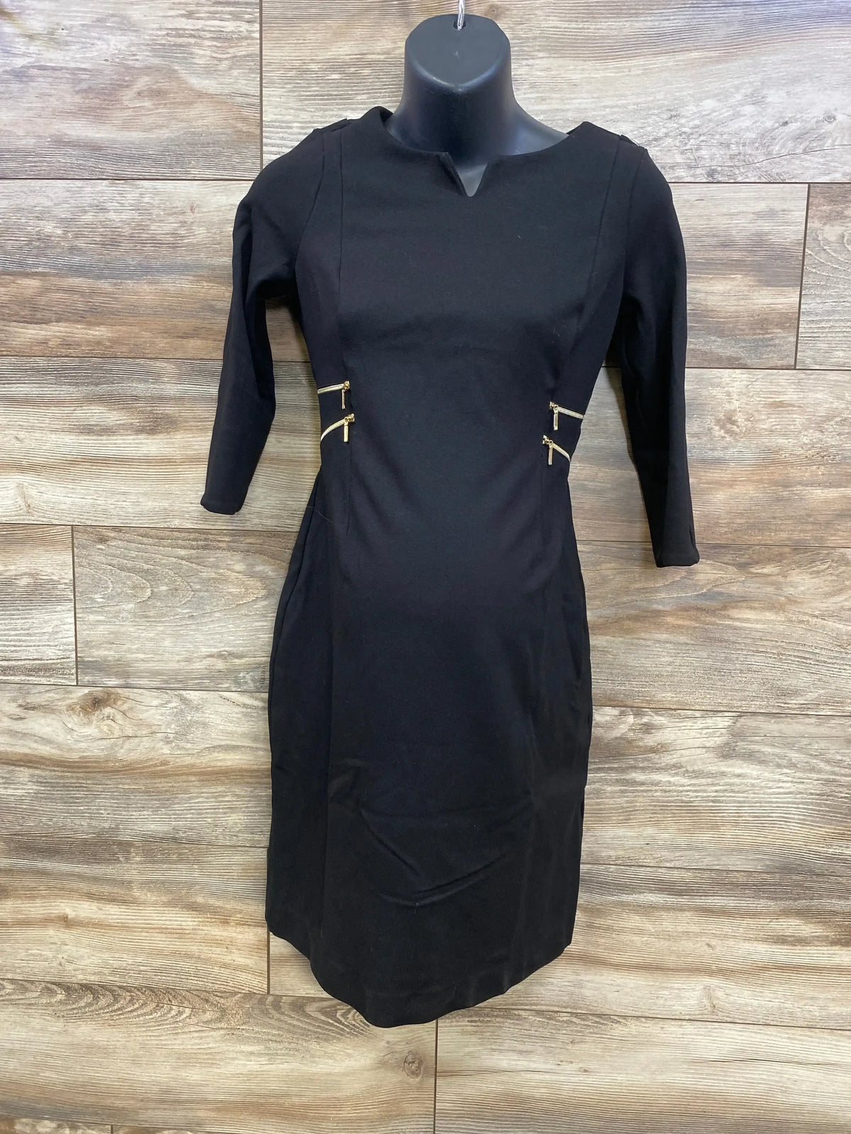 Front view of black Seraphine 3/4 sleeve maternity dress with gold side zippers on a mannequin against wood plank background