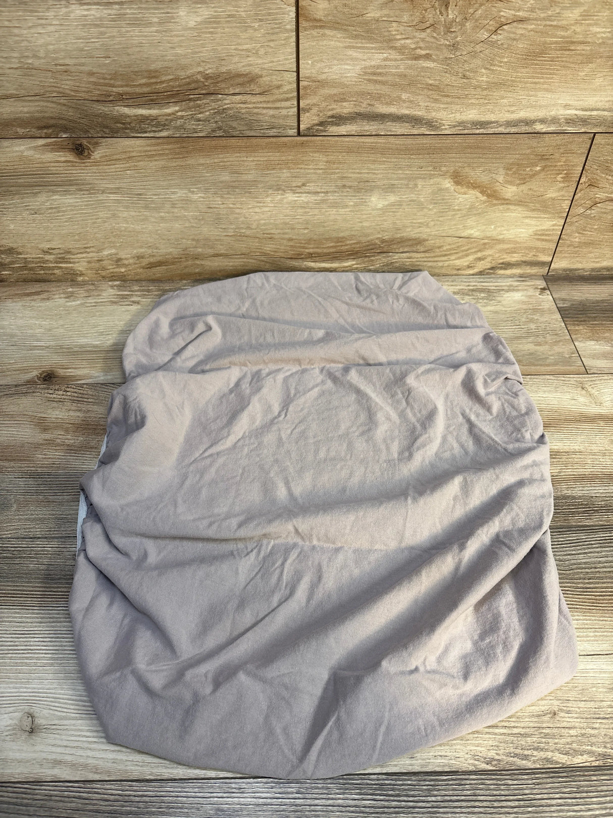 Wrinkled light gray fitted cotton sheet on wood floor background
