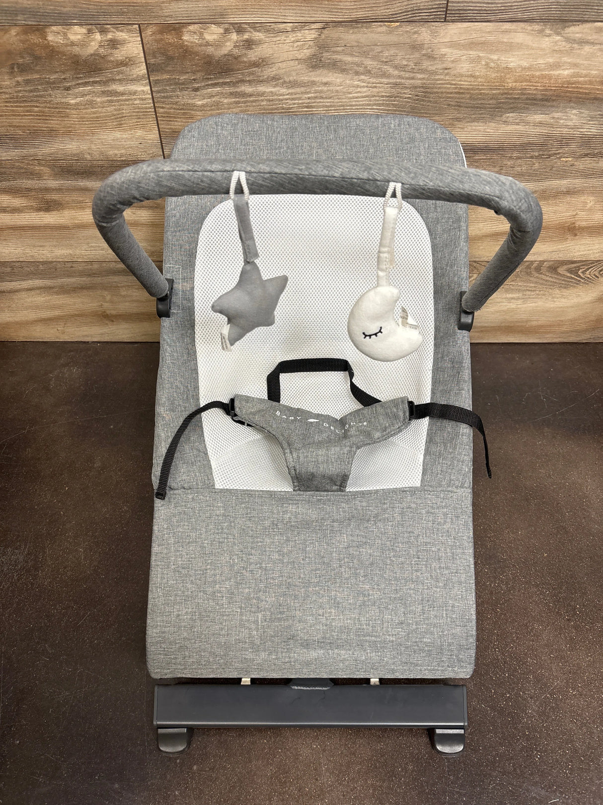 Gray baby bouncer seat with soft star and moon hanging toys on wooden floor