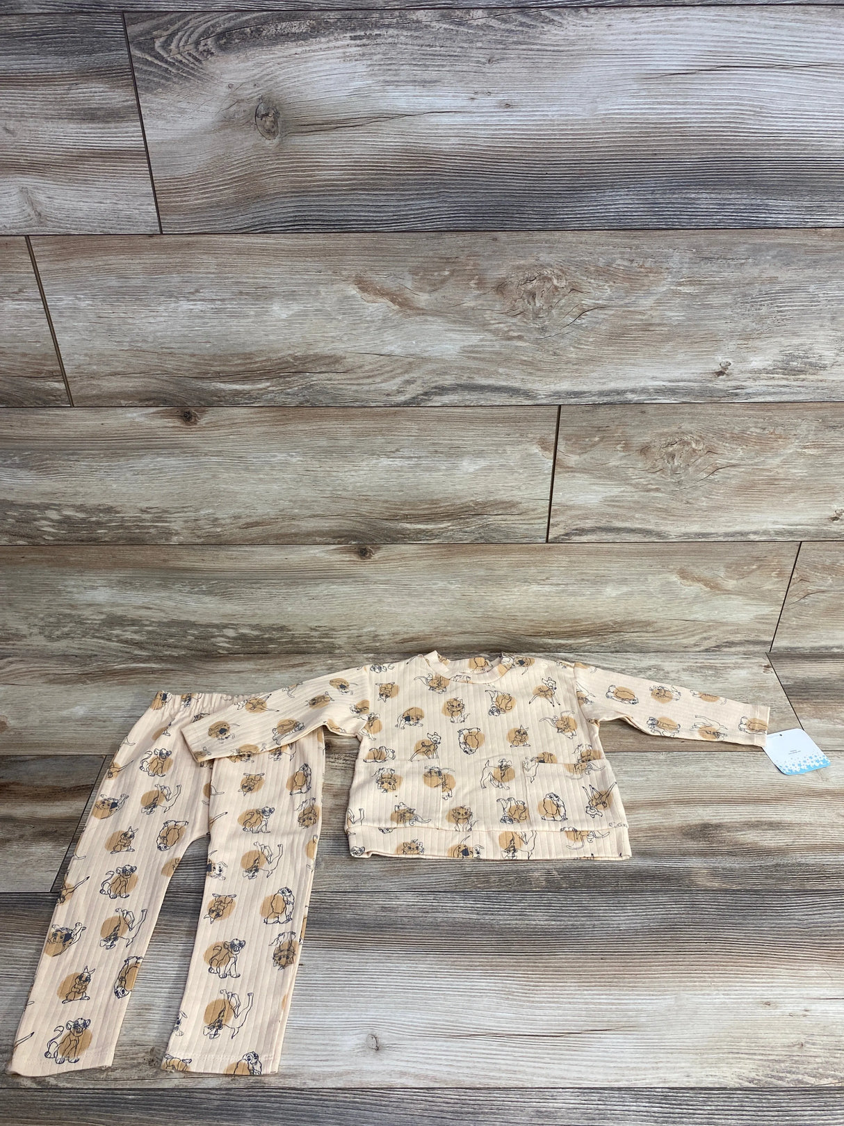 Beige ribbed kids pajamas with playful brown and black dog prints, laid flat on wood floor