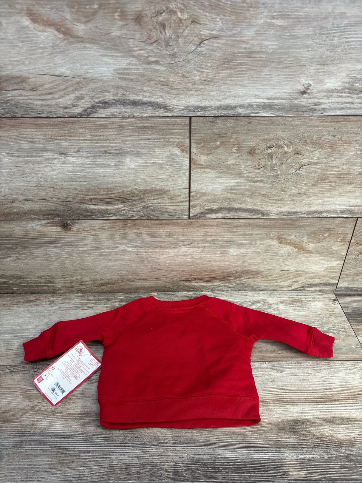 Back view of red Disney Baby Mickey Mouse sweatshirt (3-6 months) showing long sleeves and original tag on wood background